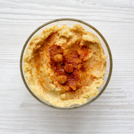 Bowl of Hummus with chickpeas, paprika and olive oil on a white wooden surface, top view. Flat lay,...