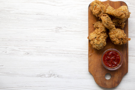 Fried chicken drumsticks with sauce on wooden board over white wooden background, top view. Overhead, flat lay, from above. Space for text.の写真素材