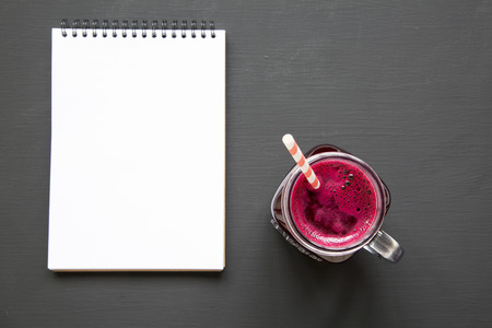 Beetroot smoothie in glass jar mug with blank notepad over black background, view from above. Flat lay, overhead. Closeup.の写真素材