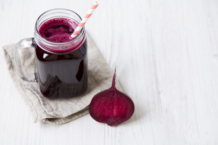 Glass jar of beetroot smoothie on white wooden table, high angle. Copy space.