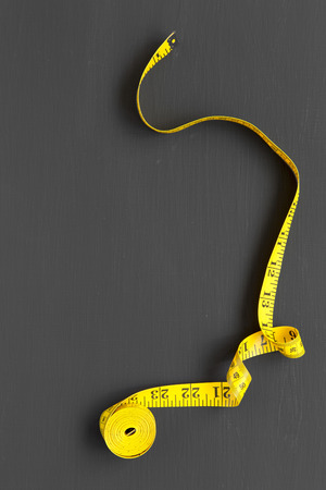 Top view, yellow measuring tape on black background. From above. Copy space and text area.