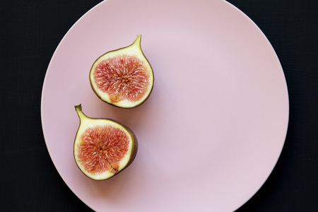 Two halves of fresh fig on pink plate over black background, top view. Flat lay, overhead.の写真素材