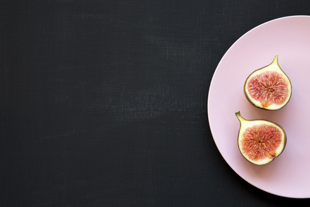 Fresh figs on pink plate over black surface, top view. Flat lay, overhead, from above. Copy space.