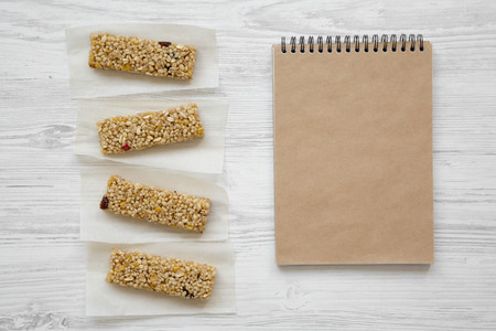Granola bars on baking sheet and blank notepad over white wooden background, top view.の写真素材