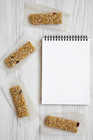 Granola bars on baking sheet and notepad over white wooden surface, top view. Space for text.の写真素材