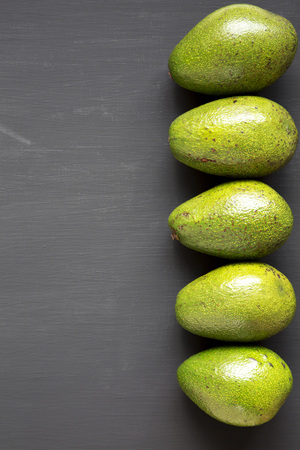 Whole avocados on black wooden background, overhead view. Top view, from above, flat lay. Space for...