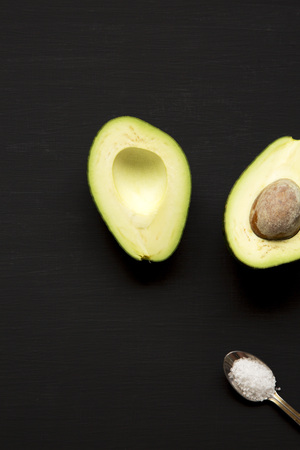 Halved avocado and sea salt on dark table, overhead view. Top view, from above.