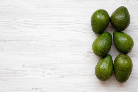 Whole avocados on white wooden table, top view. Flat lay, overhead, from above. Copy space and text...