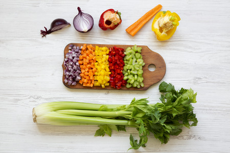 Chopped fresh vegetables (carrot, celery, onion, colored peppers) arranged on cutting board on white wooden background, top view. From above, overhead.の写真素材