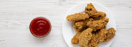 Chicken wings on a round white plate with sauce on a white wooden surface, top view. Flat lay, overhead, from above. Closeup.の写真素材