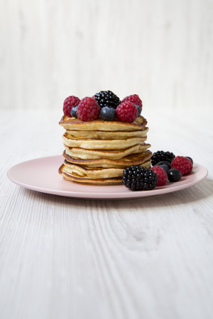 Pancakes with berries on a pink plate over white wooden background, side view.の写真素材
