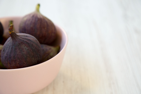 Fresh figs in a pink bowl on a white wooden background, side view. Space for text. Selective focus.の写真素材
