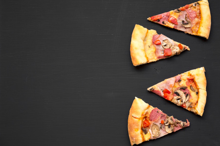 Slices of freshly baked pizza on black background, top view. Copy space.