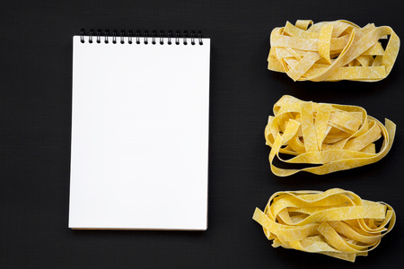Uncooked pasta pappardelle and blank notepad on black background. From above. Copy space.の写真素材