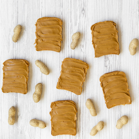 Flat lay of toasts with peanut butter and unshelled peanuts on a white wooden table. Closeup.