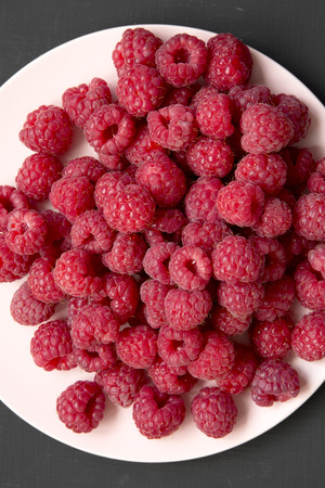 Raspberry on a pink plate on black background, overhead view. Flat lay, top view, from above....