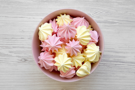 Mini meringues in a pink bowl over white wooden background, top view. Flat lay, overhead, from above.の写真素材