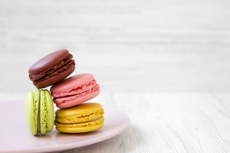 Sweet and colorful macaroons on pink plate over white wooden surface, side view. Close-up. Copy space.の写真素材