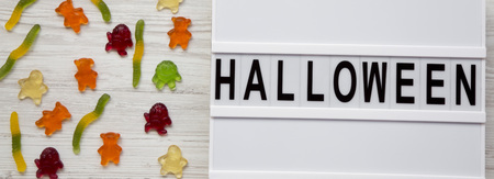 'Halloween' word on modern board, jelly monsters and worms on white wooden background, overhead view. From above, top view, flat lay.の写真素材