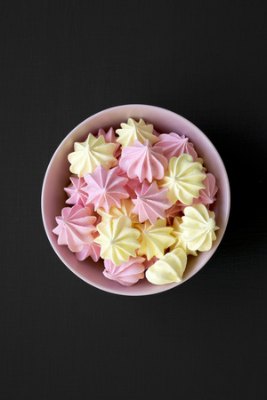 Mini meringues in a pink bowl over black background, overhead view. From above, top view. Closeup.の写真素材