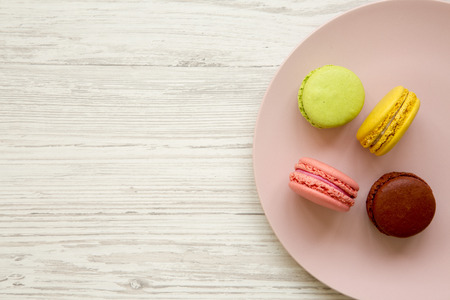Colorful macaroons on a pink plate over white wooden background, overhead view. Close-up. Copy space.の写真素材