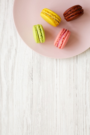 Sweet and colorful macarons on a pink plate over white wooden background, top view. Closeup. Copy space.の写真素材