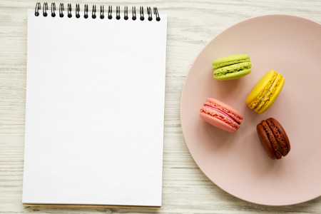 Colorful macaroons and blank notepad over white wooden background, top view. Flat lay, overhead, from above.の写真素材