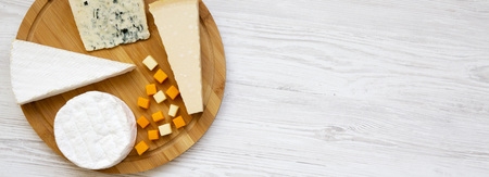 Tasting cheese on round bamboo board on a white wooden table. Food for wine, top view. Flat lay,...