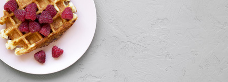 Traditional belgian waffle with raspberries on pink plate over concrete background, top view. Space...