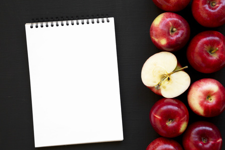 Fresh raw red apples and blank notebook on black background, top view. Flat lay, overhead, from...
