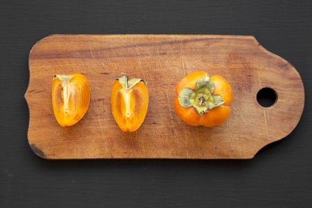 Fresh persimmon on rustic wooden board over black surface, overhead view. Flat lay, top view, from above.の写真素材