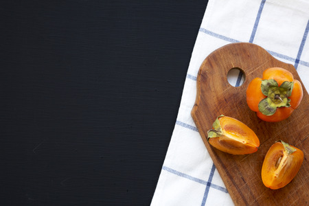 Fresh persimmon on rustic wooden board over dark background, top view. Flat lay, overhead, from above. Copy space.の写真素材