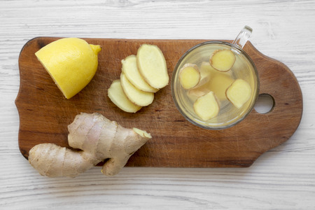 Mug of homemade ginger tea with lemon on wooden board over white wooden background, overhead view. Close-up.の写真素材