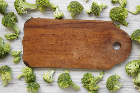 Freshly cut raw broccoli and rustic wooden board on white wooden background, overhead view. Flat lay, from above, top view.の写真素材