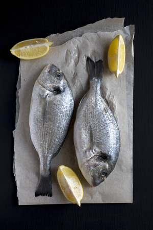 Fresh dorado fish with lemon on baking sheet over dark background, overhead view. Flat lay, from above, top view.の写真素材