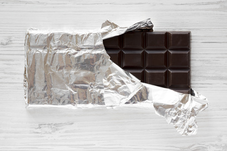 Dark chocolate in a wrapper over white wooden background, overhead view. Flat lay, from above, top view.の写真素材