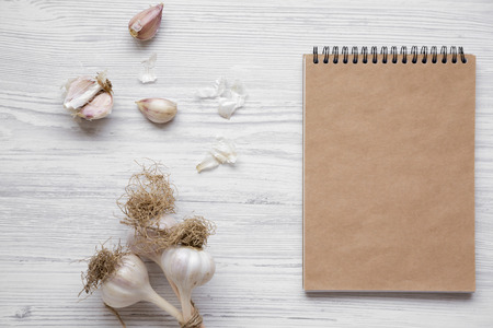 Garlic cloves, garlic bulbs and blank notepad on white wooden background, overhead view. From above, top view.の写真素材