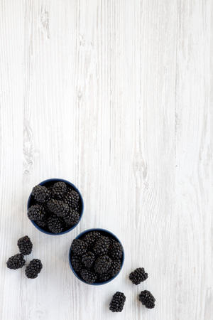 Full blue bowls of blackberries over white wooden background, overhead view. Summer berry. From above, top view. Copy space.の写真素材