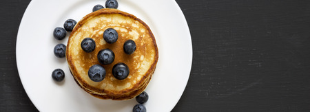 Pancakes with blueberries on a white round plate over dark background, top view. Copy space. Flat lay, overhead, from above.の写真素材