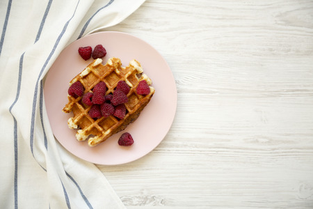 Traditional belgian waffle with raspberries on pink plate over white wooden background, overhead view. Copy space.の写真素材