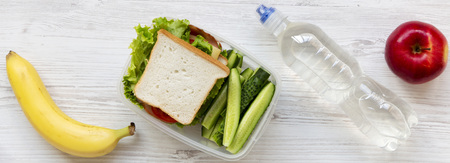 School lunch box with sandwich, fruits and bottle of water on white wooden background, flat lay....