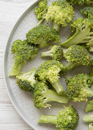 Freshly cut raw broccoli on gray plate over white wooden surface, top view. Flat lay, from above, overhead.の写真素材