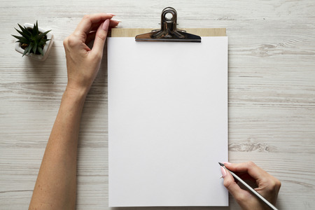 Feminine workspace with female hands, clipboard and sheet of paper, overhead. Top view.の写真素材
