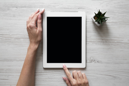 Female hands using tablet over white wooden background, overhead view. Top view, from above.の写真素材