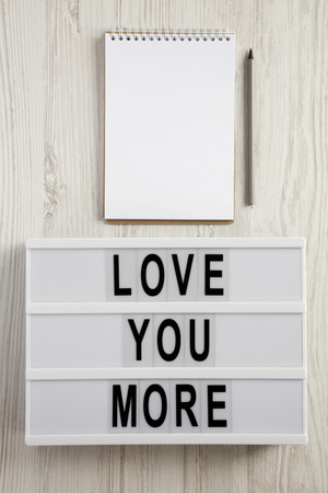 Modern board with text 'Love you more', blank notepad and pencil on a white wooden background. Valentine's Day 14 February.の写真素材