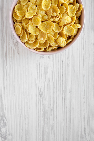 Crispy corn flakes in a pink bowl for breakfast on a white wooden table, top view. Flat lay,...