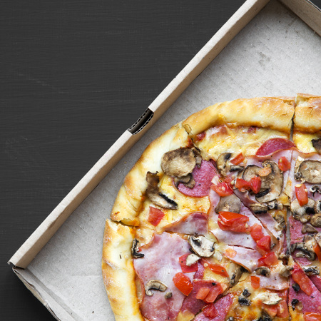 Freshly baked pizza in a cardboard box on black background, overhead view. Flat lay, top view, from above.の写真素材