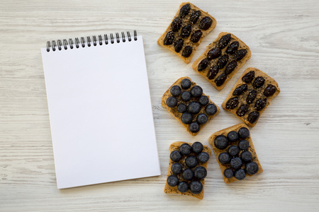 Vegan toasts with peanut butter, blueberries, olives and chia seeds on a white wooden table,...