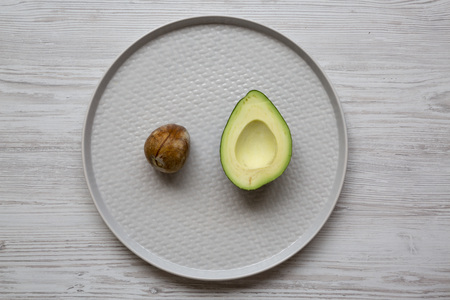 Half avocado with bone on plate over white wooden background, top view. Overhead, from above, flat lay.の写真素材