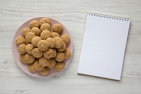 Almond cookies on pink plate, blank notepad over white wooden background, overhead. view. Flat lay, top view.の写真素材